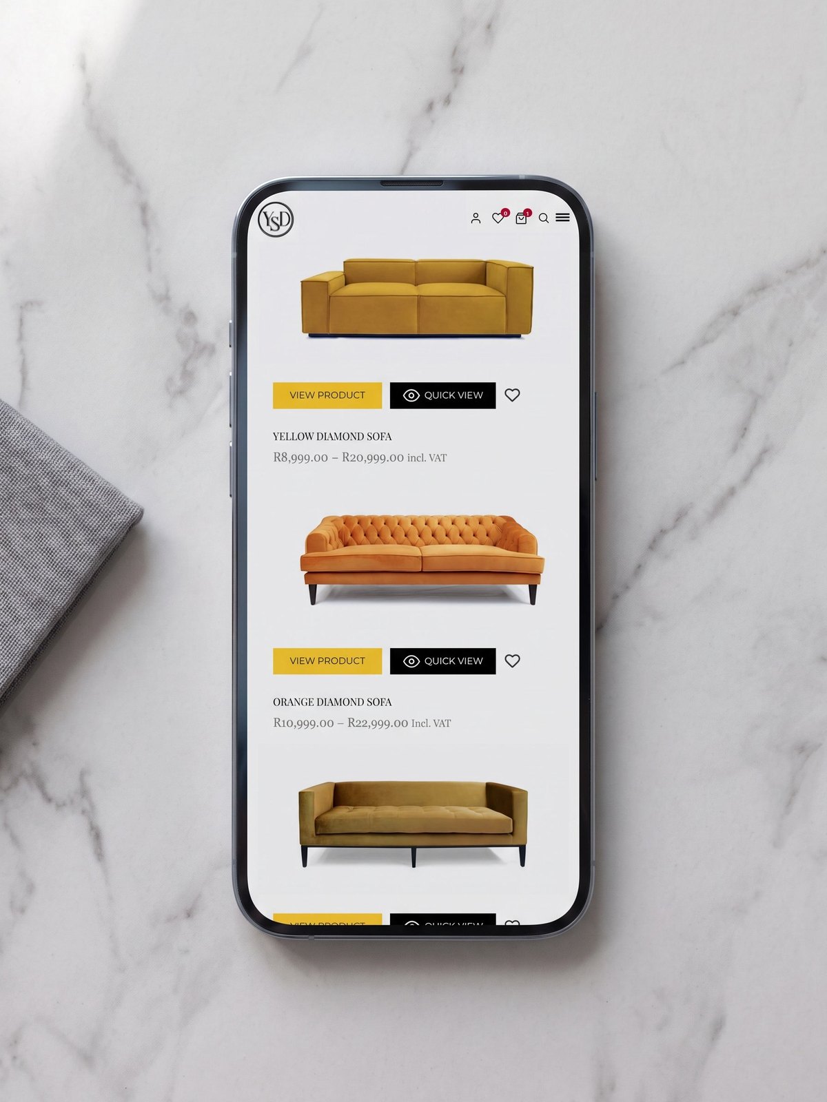 A phone lying on pale marble, its screen showing the Yellowstone Design mobile shop with velvet sofas listed beneath the YSD monogram.